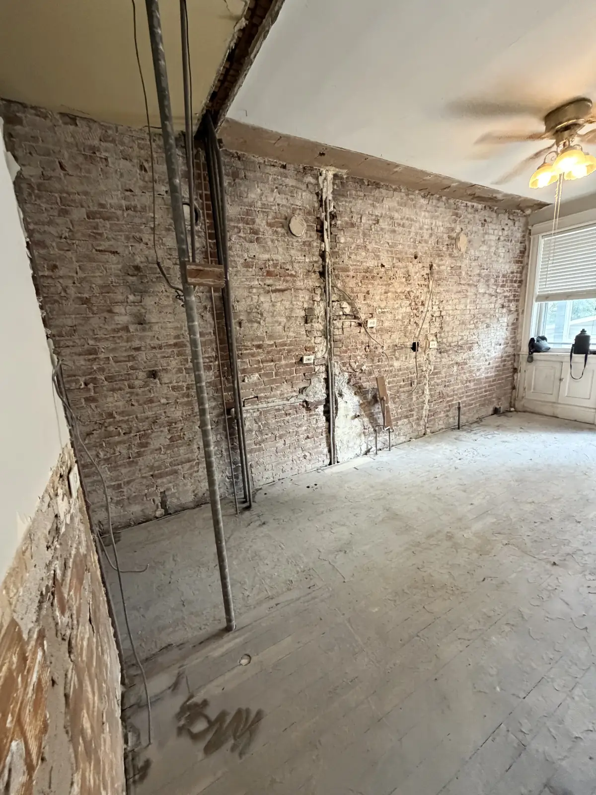 Kitchen gutted to the bare brick wall and floorboards after interior demolition, old pipes and wiring exposed