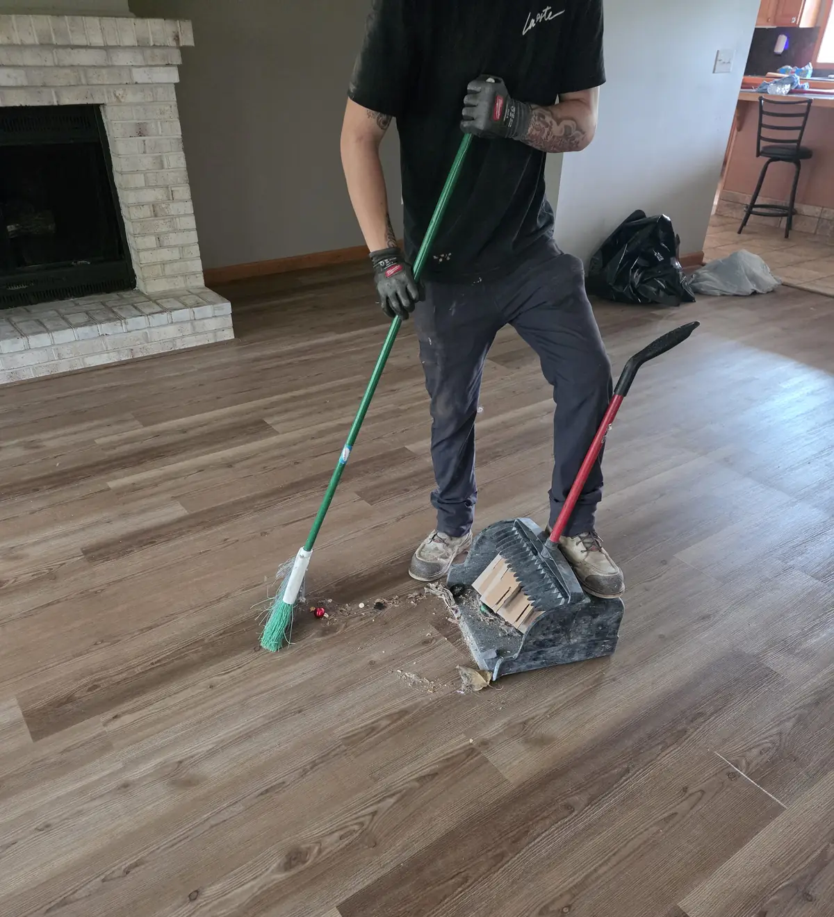 Crew member in work gloves sweeping debris into a dustpan on a cleared living room floor
