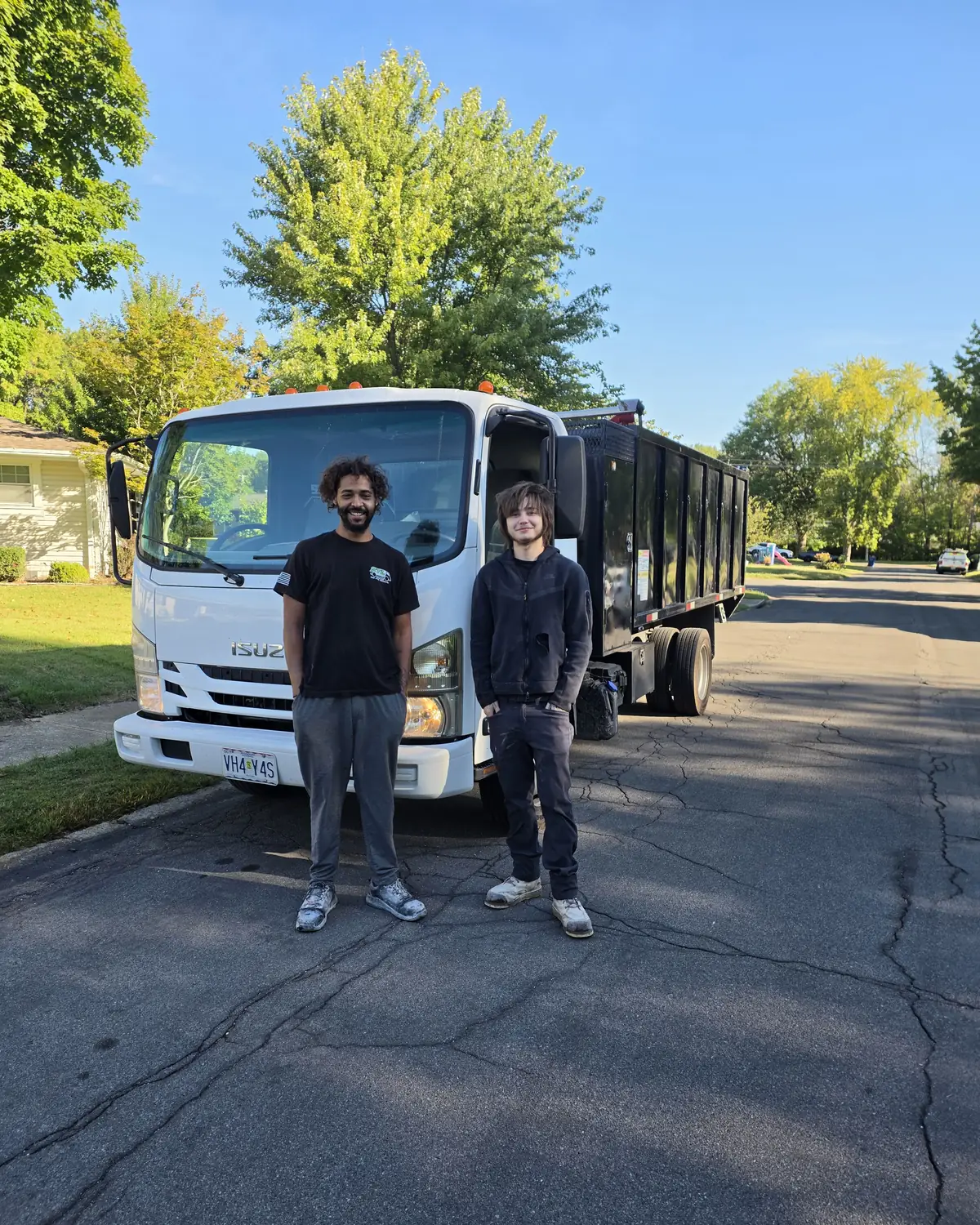 Two crew members standing in the street in front of the white Isuzu junk removal truck